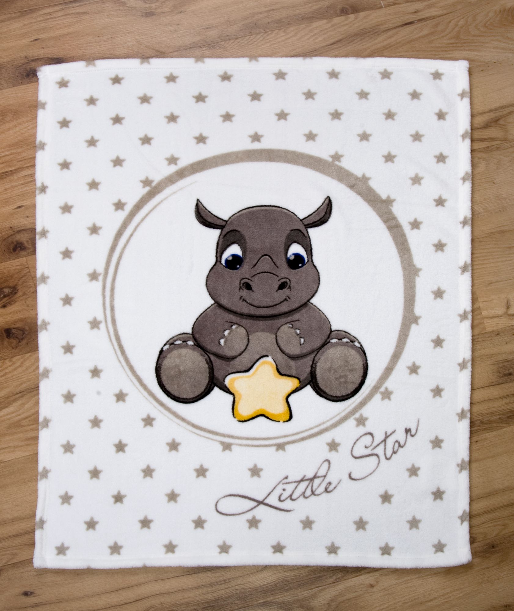 Draufsicht der Babydecke flach ausgebreitet auf hellem Holzboden; zeigt die gesamte Vorderseite mit dem Nashorn-Motiv und dem Sternen-Hintergrund in einer zentrierten, geraden Ansicht.