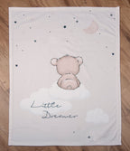 Draufsicht der Baby-Kuscheldecke komplett flach ausgebreitet auf hellem Holzboden; zeigt das zentrale Motiv des kleinen Bären, der von hinten auf einer Wolke sitzt, den Schriftzug „Little Dreamer“, Wolken, Sterne und eine Mondsichel.