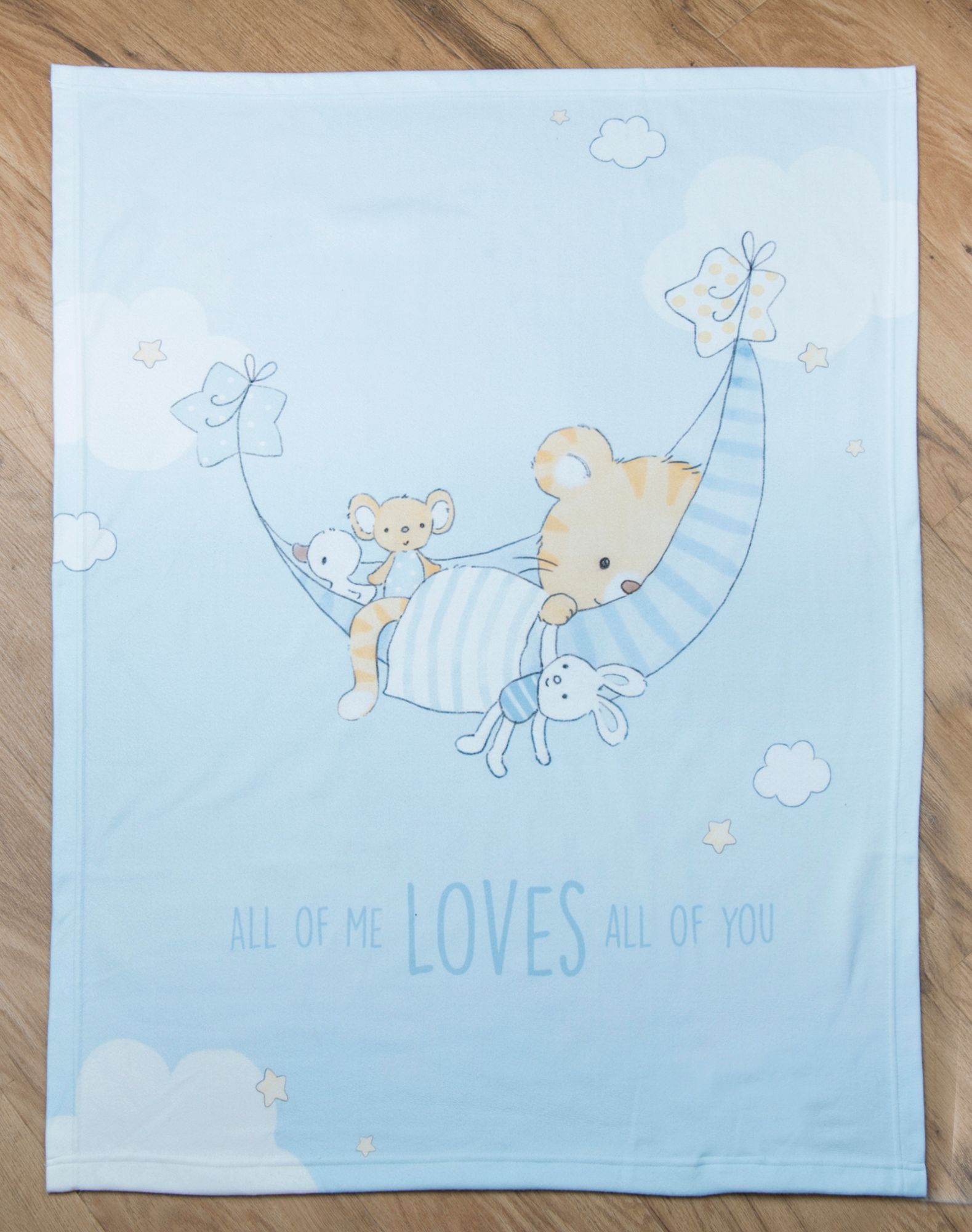 Draufsicht der Babydecke flach ausgebreitet auf hellem Holzboden; zeigt den schlafenden Tiger mit seinen Kuscheltieren in einer Hängematte und den Spruch „ALL OF ME LOVES ALL OF YOU“.