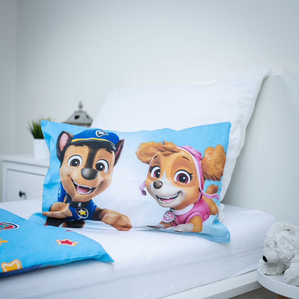 Nahaufnahme des aufgestellten Kopfkissens auf einem weißen Bett; zeigt die beiden Paw Patrol Charaktere Chase und Skye vor einem hellblauen Hintergrund.