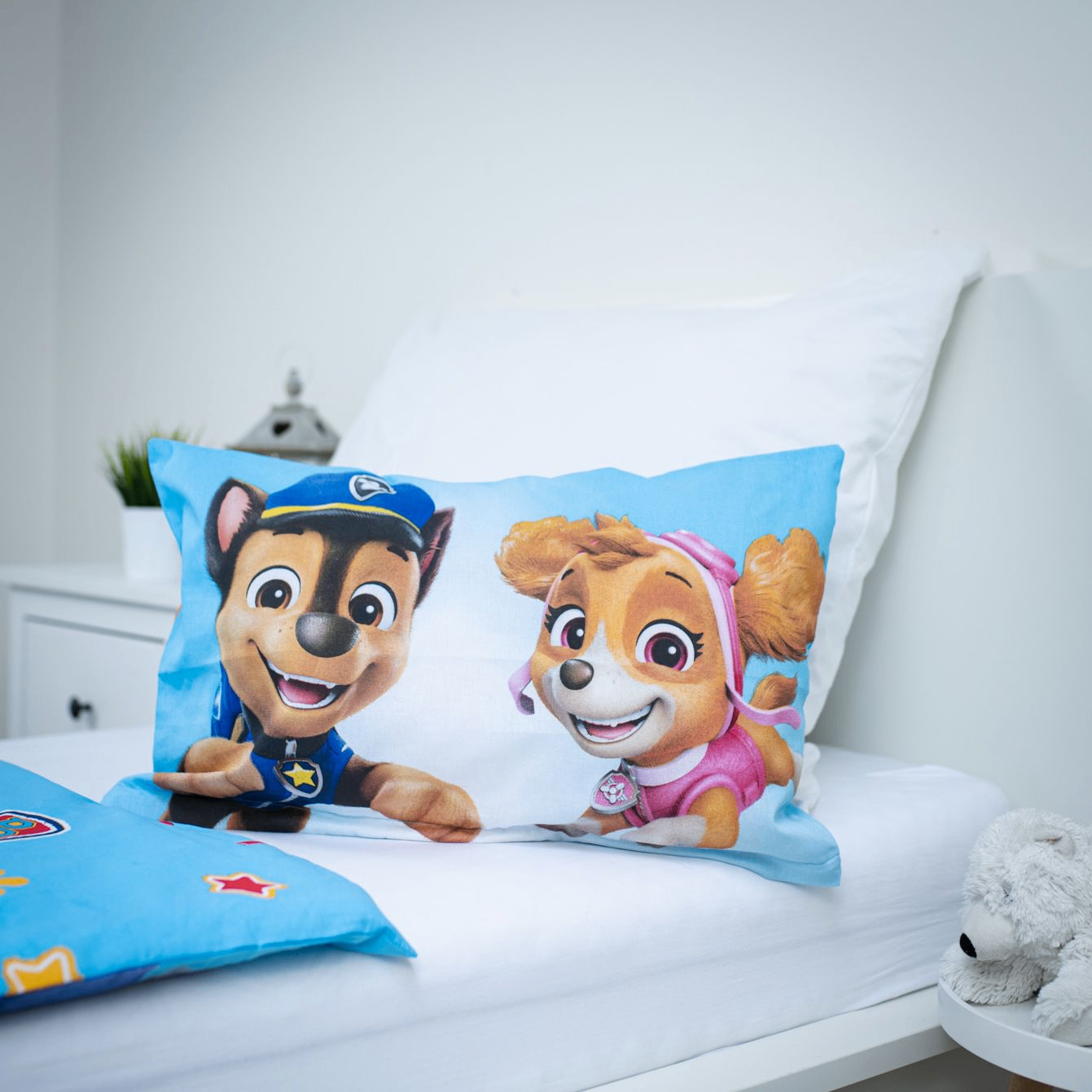 Nahaufnahme des aufgestellten Kopfkissens auf einem weißen Bett; zeigt die beiden Paw Patrol Charaktere Chase und Skye vor einem hellblauen Hintergrund.