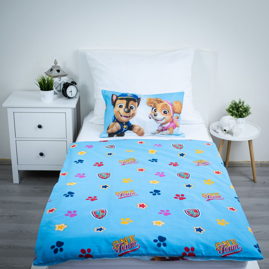 Ambiente-Aufnahme des komplett bezogenen Kinderbettes; präsentiert die hellblaue Wendeseite des Bettbezugs mit dem Allover-Muster aus Sternen, Pfoten und dem „ONE Team“-Schriftzug.