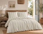 Helles Schlafzimmer mit komplett bezogenem Bett in blau-gestreifter Leinen-Bettwäsche, hölzernem Kopfteil und mediterraner Deko.