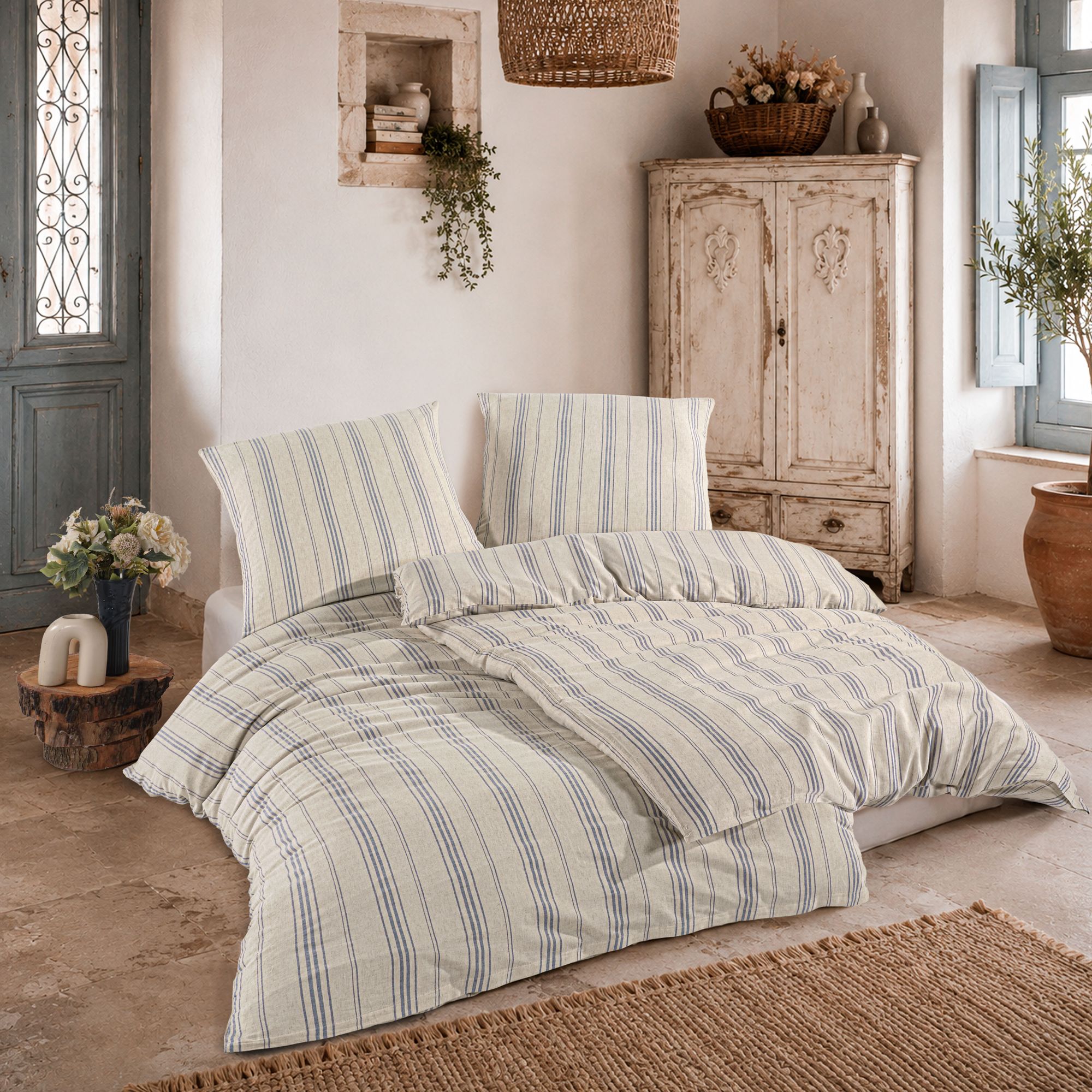 Bett mit blau-beiger Streifen-Bettwäsche auf Fliesenboden, flankiert von antikem Schrank und Pflanzen.