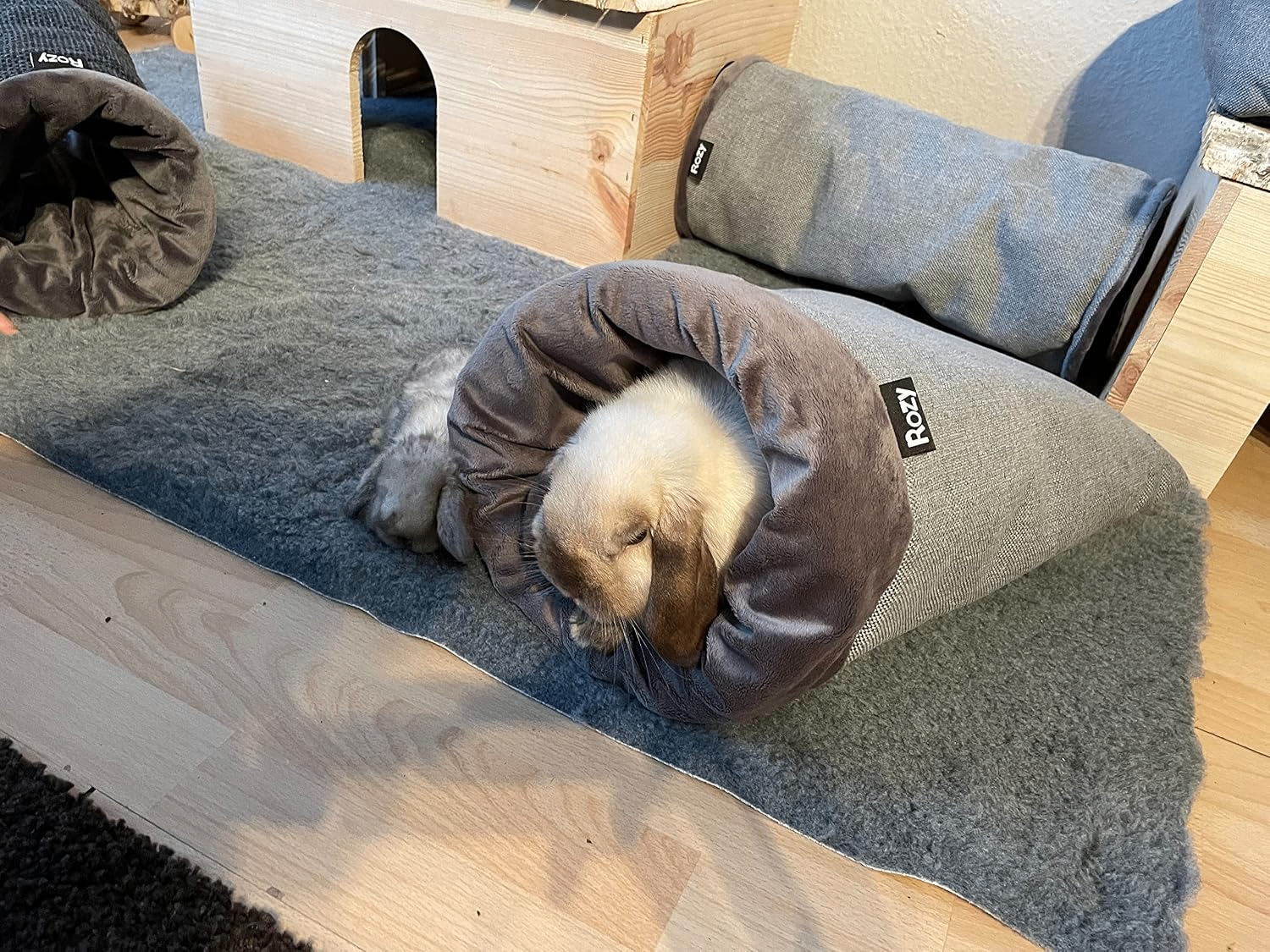 Nahaufnahme: Der kegelförmige „Rozy“-Kuschelsack mit Plüschfutter. Ein helles Kaninchen liegt im Sack, das dunklere, kleinere Kaninchen ruht entspannt davor.