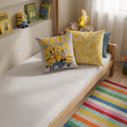 Dekoriertes Kinderbett aus Holz mit beiden Wendemotiven des Minions-Kissens und buntem Teppich.
