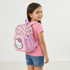 Mädchen von der Seite mit dem rosa Hello Kitty Kinderrucksack auf dem Rücken vor hellgrauem Hintergrund.