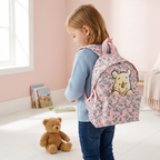 Mädchen von der Seite mit dem rosa Winnie Puuh Kinderrucksack auf dem Rücken vor hellgrauem Hintergrund.