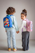 Zwei Kinder von hinten, die sich an den Händen halten, mit einem blauen und einem rosa Rucksack.