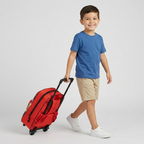 Ein fröhlicher Junge im blauen T-Shirt zieht den roten Cars 3D Trolley Rucksack Piston Cup Kinder-Trolley Rot 38 cm hinter sich her.