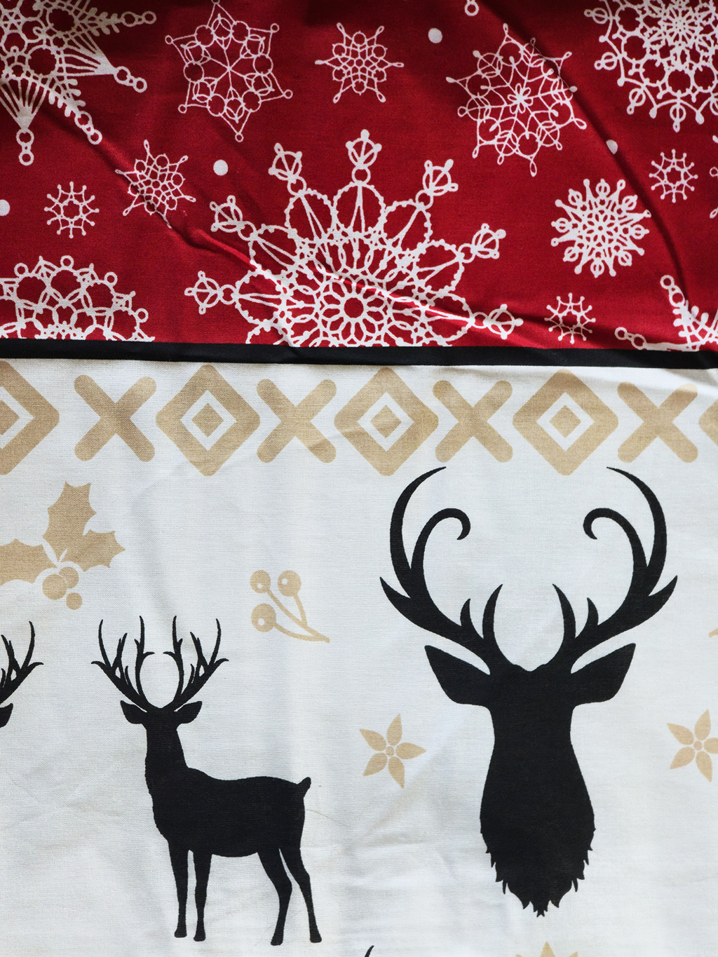 Detailansicht einer Bettwäsche-Oberfläche mit rotem und weißem Bereich; oben mit weißen schneeflockenartigen Mustern auf rotem Grund, unten mit schwarzen Hirschsilhouetten, goldenen Akzenten und einer X-Muster-Borte auf hellem Grund.